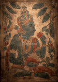 Stylized blue figure wearing ornate crown holds a flower and round fruit, surrounded by leaves.