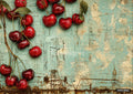 Cherries with green leaves and thin brown stems hang over a distressed wooden surface painted blue and peeling to light brown.
