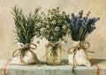 Three green bunches with white and purple blooms tied in cloth sacks and a glass jar, set on a striped tablecloth.